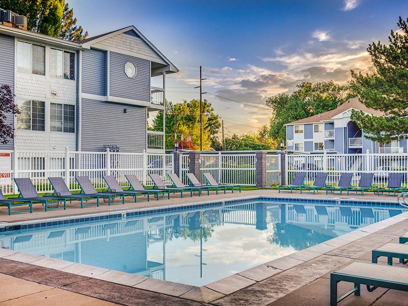 Midvale, UT Apartments - Creekview - Fenced Pool with Lounge Chairs surrounded by Apartment Buildings.