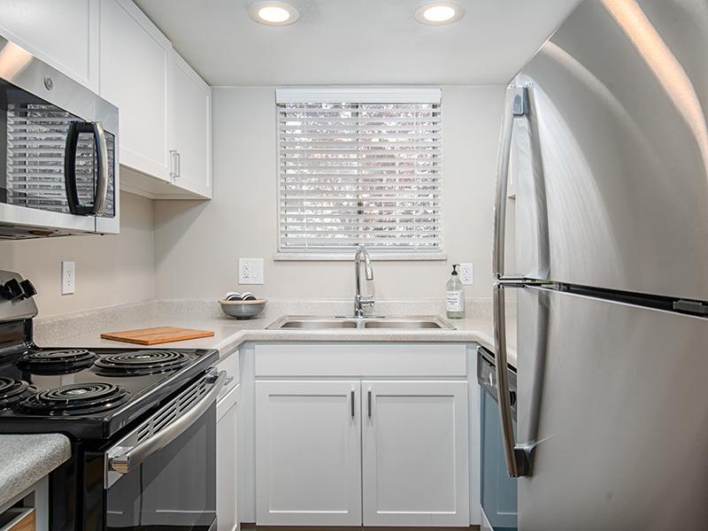 Apartments for Rent in Midvale - Creekview - Kitchen with White Cabinets, Stainless Steel Appliances, and Small Window Above Sink.