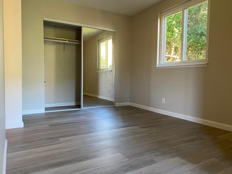 Apartments in San Rafael for Rent - Park Hill Studios - Bedroom with Mirrored Closet, Window, and Wood-Style Flooring.