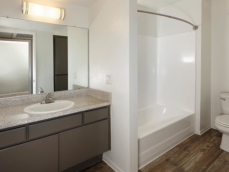 Santa Fe Springs, CA Apartments - Costa Azul Senior - Bathroom With Tub And Shower Combo, A Vanity Area With Large Mirror, and Wood-Style Flooring