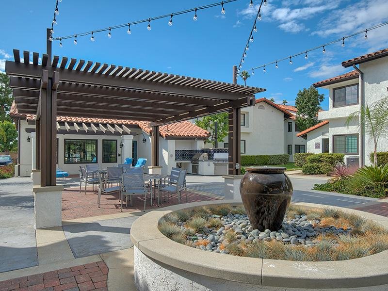 Santa Fe Springs, CA, Apartments for Rent - Costa Azul Senior - Outdoor Lounge Area Next To A Water Feature with Overhead Covering, Tables, Chairs, an