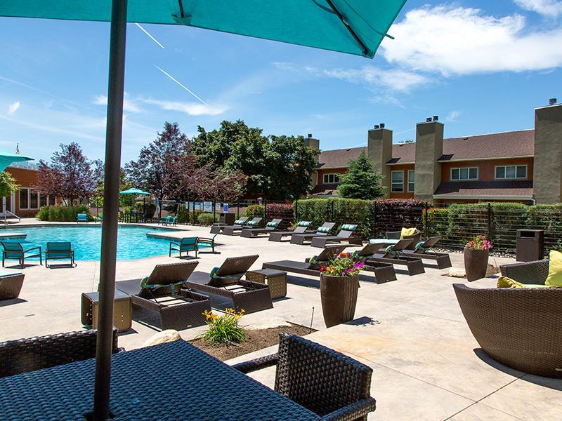 Luxury Apartments in Salt Lake City, UT - Foothill Place - Gated Pool Area with Lounge Chairs, Blue Patio Umbrellas, and Potted Plants