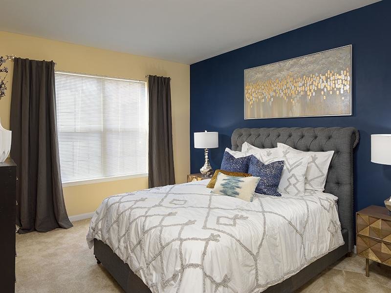 Carpeted bedroom with double window is furnished with a large bed and 2 nightstands at Colton Creek Apartments.